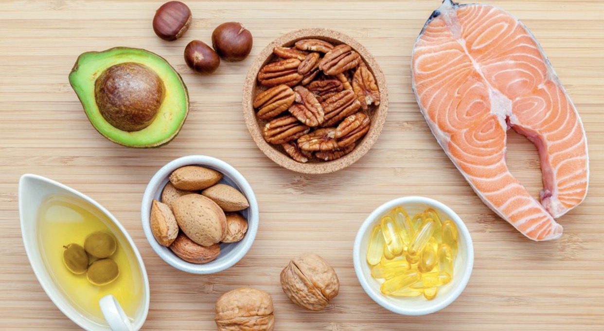 Healthy fats like salmon, avocado, olive oil and nuts on a counter top.